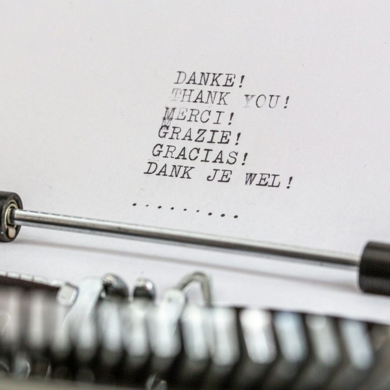 Close-up of a typewriter with a sheet of paper that reads “THANK YOU! DANK JE WEL!” typed in capital letters.